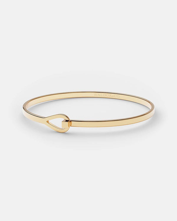 A polished stainless steel bangle in 14k gold from Waldor & Co. The model is Signature Bangle Polished