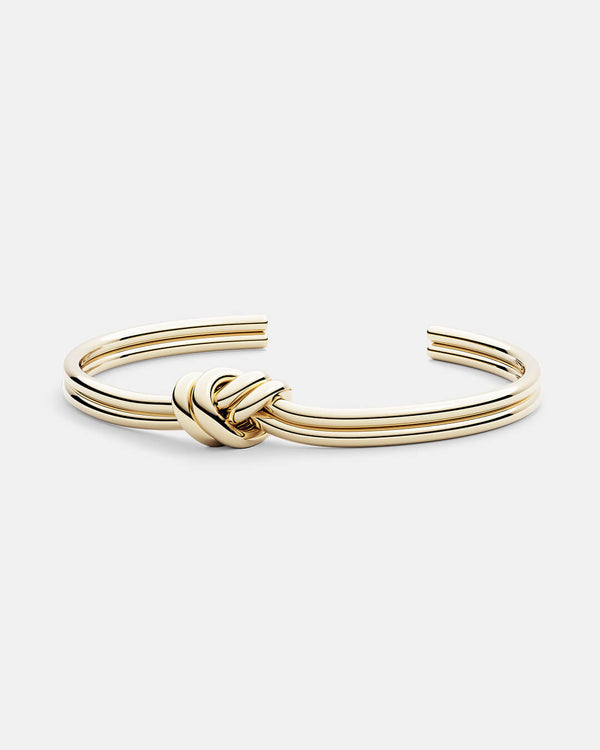 A polished stainless steel bangle in 14k gold from Waldor & Co. One size. The model is Dual Knot Bangle 