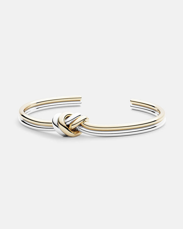 A polished stainless steel bangle in 14k gold from Waldor & Co. One size. The model is Dual Knot Bangle.