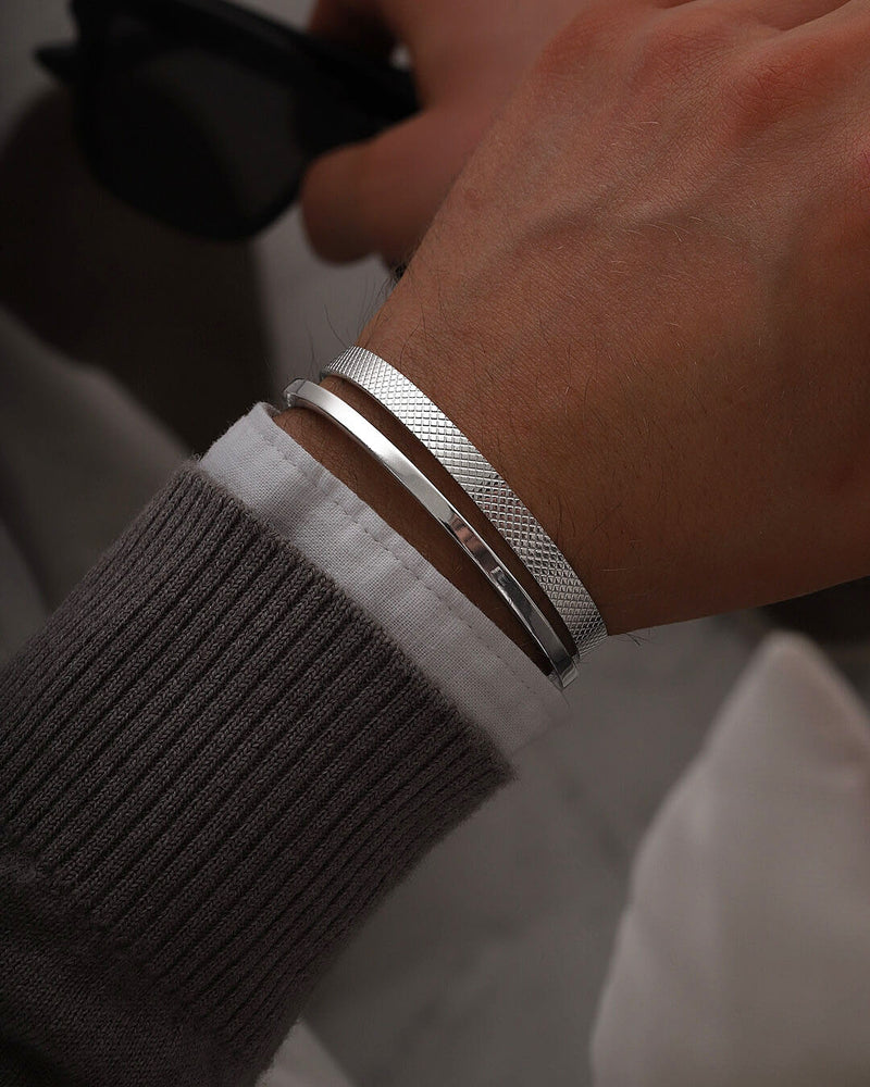 A polished stainless steel bangle in silver from Waldor & Co. One size. The model is Square Bangle Polished